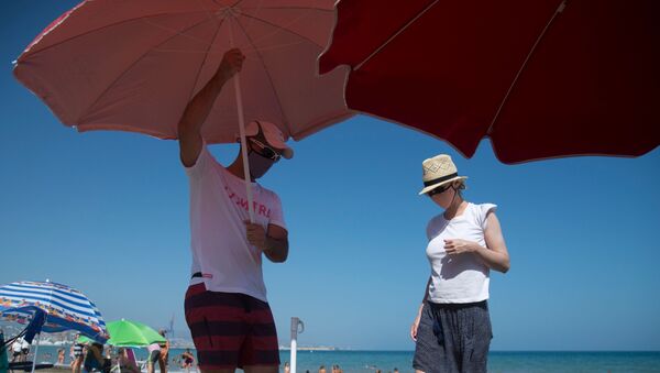 Una pareja coloca una sombrilla en una playa de Málaga - Sputnik Mundo