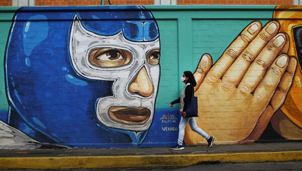 Una mujer que usa una mascarilla pasa frente a un grafiti de un luchador en México - Sputnik Mundo