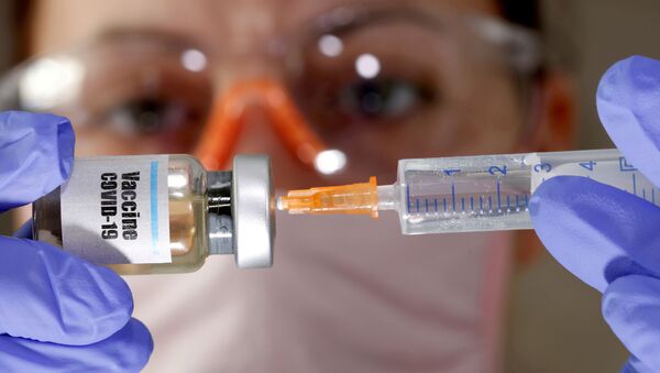 Una mujer sostiene una jeringa médica y un frasco con una etiqueta en la que se lee Vacuna COVID-19 (imagen ilustrativa) - Sputnik Mundo