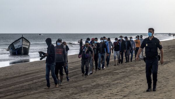 Migrantes de Marruecos caminan por la orilla escoltados por la Policía española tras llegar a la costa de Canarias - Sputnik Mundo