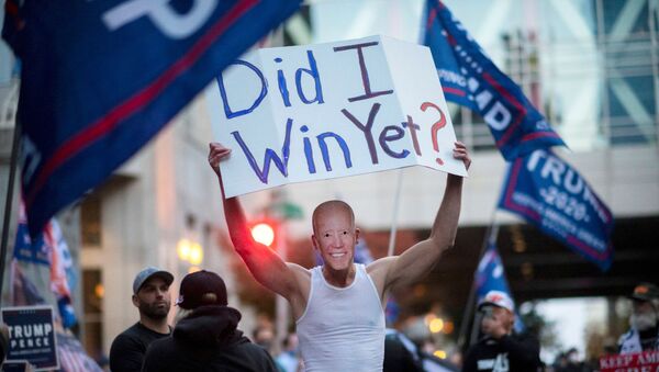 Un partidario de Trump lleva un cartel y una máscara del candidato presidencial demócrata Joe Biden durante una protesta en Filadelfia - Sputnik Mundo
