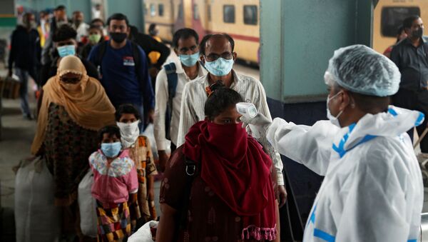 Un trabajador de la salud revisa la temperatura de los pasajeros en una estación de tren de Mumbai, la India. - Sputnik Mundo