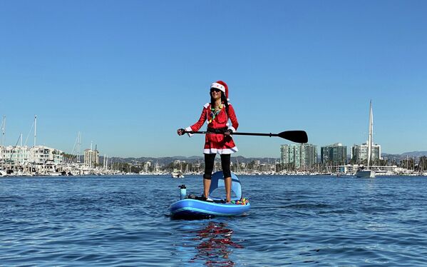 Una joven vestida de Santa Claus practica el surf de pala cerca de la costa de Los Ángeles, California. - Sputnik Mundo
