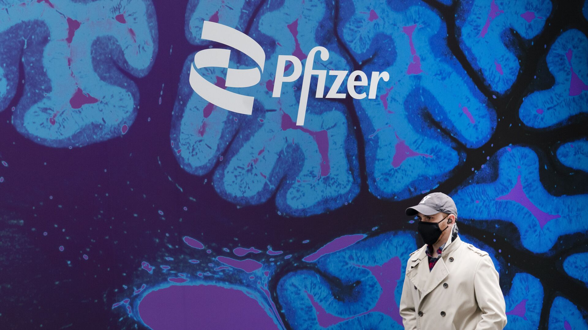 Un hombre camina frente a un logo del laboratorio de Pfizer frente a la sede del laboratorio en Nueva York - Sputnik Mundo, 1920, 09.02.2021