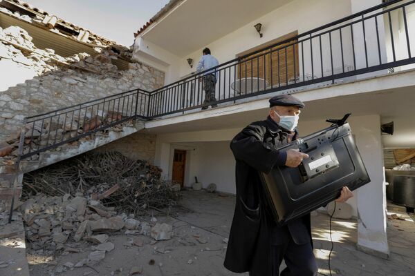 Un hombre lleva un televisor que se quedó intacto de su casa destruida por un terremoto en el pueblo de Damasi en Grecia Central. - Sputnik Mundo