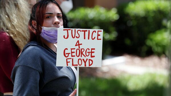Un manifestante sostiene un cartel que dice Justicia para George Floyd cerca de la casa del exoficial de policía Derek Chauvin - Sputnik Mundo