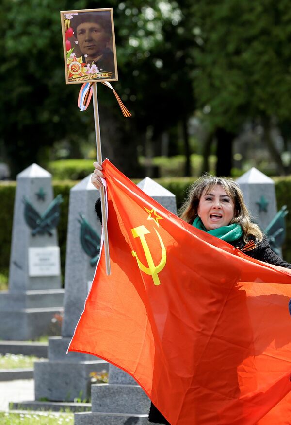 Una mujer sostiene una bandera y canta frente a las tumbas de soldados rusos en el cementerio de Olsany, en la capital de la República Checa, para conmemorar el 76 aniversario del fin de la Segunda Guerra Mundial.   - Sputnik Mundo