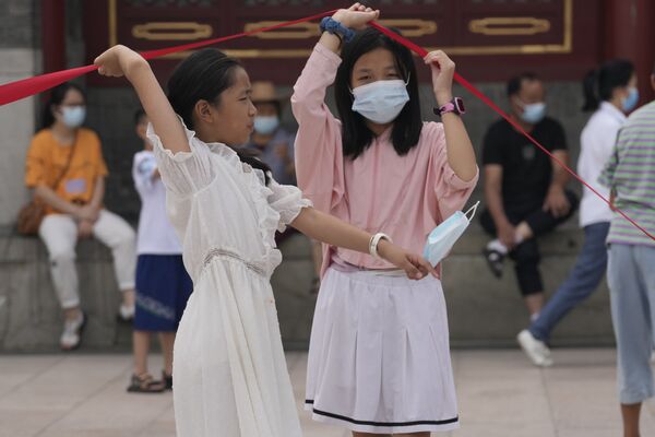 La variante delta del coronavirus está desafiando la costosa estrategia china de imponer un aislamiento casi total en cualquier foco. En la foto: dos niñas con mascarillas levantan una barrera en Pekín. - Sputnik Mundo