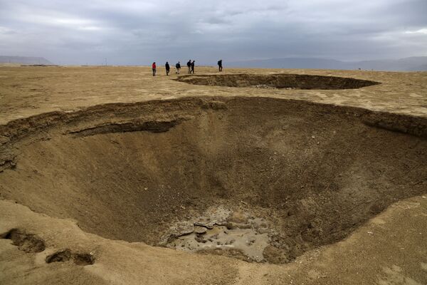 Algunos de los cráteres, bautizados como dolinas, llegan a medir más de 10 metros de profundidad. Hay miles de agujeros en la costa del mar Muerto. En la foto: unos turistas en un valle salado ubicado a unos 20 kilómetros al sur de la comuna agrícola israelí de Ein Gedi, construida en una parte seca del mar Muerto. - Sputnik Mundo