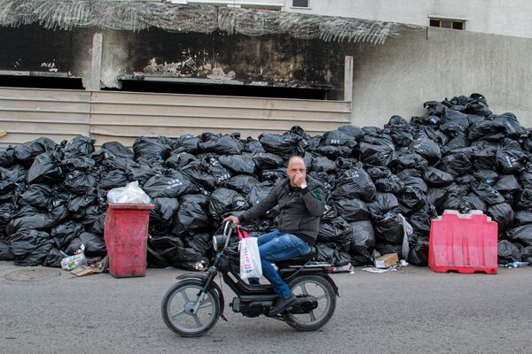 Un hombre se tapa la nariz mientras conduce una motocicleta cerca de sacos de basura apilados a lo largo de un muro en el centro de la ciudad costera de Sfax (Túnez).  El 6 de noviembre, los residentes y las ONG lanzaron un grito de alarma ante lo que describieron como una falla en la gestión de residuos en la ciudad. Montañas de bolsas de basura, malolientes y cubiertas de moscas, se han ido acumulando en diferentes distritos de la ciudad durante más de 40 días, incluso cerca de hospitales, tiendas y escuelas. - Sputnik Mundo