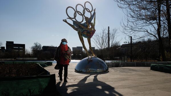 Una mujer pasa cerca de una estatua con los Anillos Olímpicos frente a la sede del Comité Organizador de los Juegos Olímpicos y Paralímpicos de Invierno de Beijing 2022 en el Parque Shougang, en Pekín, China, el 30 de noviembre de 2021 - Sputnik Mundo