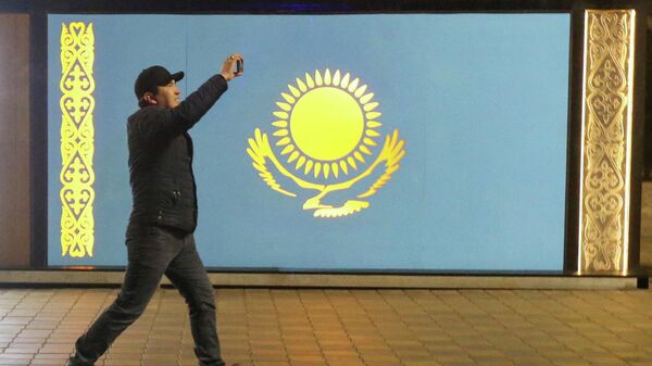 Un hombre pasa frente a la bandera de Kazajistán durante las protestas en Almaty - Sputnik Mundo