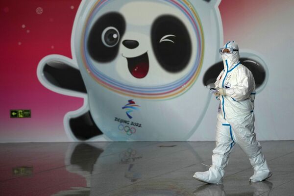 Un funcionario médico con traje de protección en el aeropuerto de Shawdue, en Pekín. En el fondo hay una imagen de la mascota oficial de los Juegos Olímpicos de Invierno de 2022, el panda Bing Dong. - Sputnik Mundo
