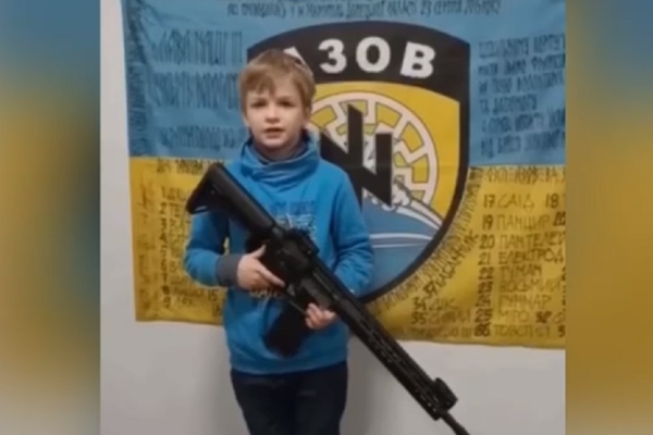 Un niño ucraniano con un fusil posa frente a un símbolo nazi, captura de pantalla - Sputnik Mundo