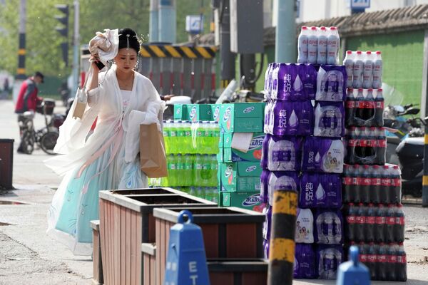 Una mujer vestida con un traje tradicional pasa cerca del comercio de bebidas abandonados a lo largo de una carretera, en Pekín. - Sputnik Mundo