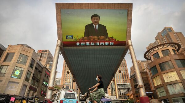 Una mujer pasa en bicicleta junto a una gran pantalla de televisión en un centro comercial, que emite un reportaje de la televisión china sobre la visita de Xi Jinping a Hong Kong - Sputnik Mundo