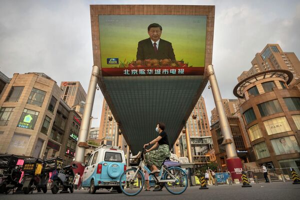 Una mujer en bicicleta pasa por delante de una enorme pantalla de televisión instalada en el exterior de un centro comercial en Pekín, China, mientras se retransmite un discurso del líder chino Xi Jinping, que está de visita en Hong Kong. - Sputnik Mundo