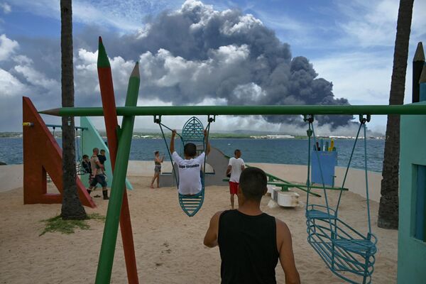 Niños juegan en un parque de la provincia de Matanzas, Cuba, con el humo negro al fondo tras el incendio masivo de un depósito de petróleo. - Sputnik Mundo