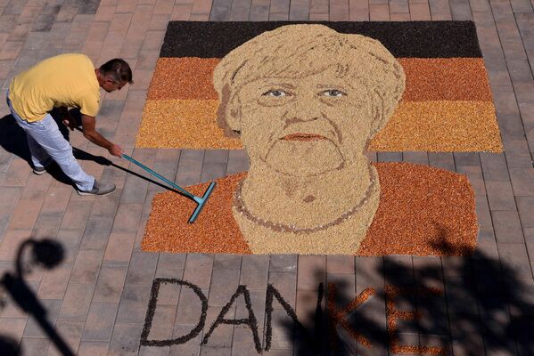 En vísperas de la dimisión de la canciller alemana Angela Merkel el artista kosovar Alkent Pozhegu completa su retrato en la plaza de la ciudad de Gjakova, creándolo con semillas y granos. En vísperas de la dimisión de la canciller alemana Angela Merkel el artista kosovar Alkent Pozhegu completa su retrato en la plaza de la ciudad de Gjakova, creándolo con semillas y granos. - Sputnik Mundo