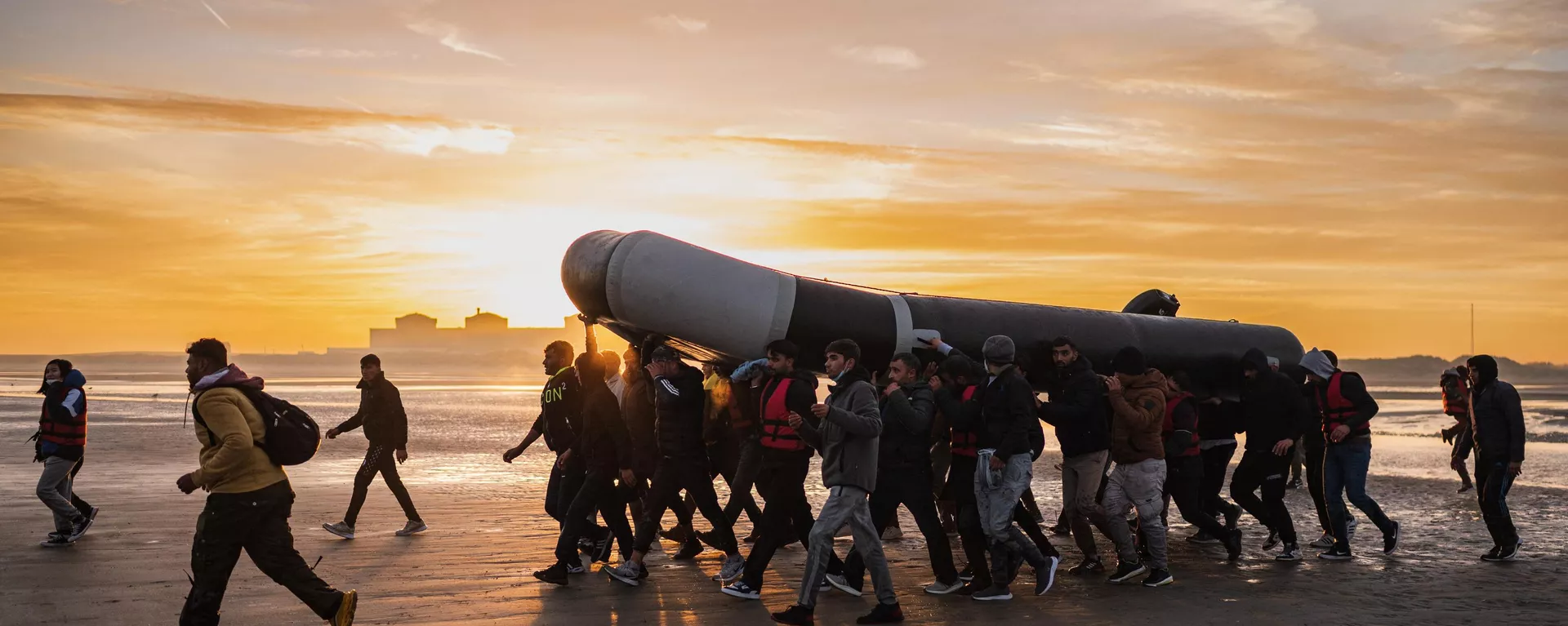 Migrantes llevan a hombros una embarcación de contrabando mientras se preparan para embarcar en la playa de Gravelines, cerca de Dunkerque, en el norte de Francia, el 12 de octubre de 2022, en un intento de cruzar el canal de la Mancha.  - Sputnik Mundo, 1920, 18.12.2022