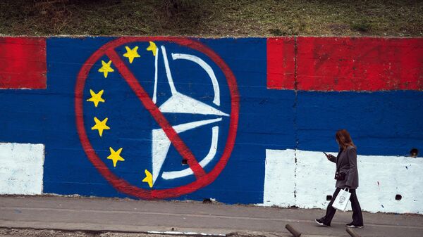 Una persona camina junto a un mural contra la UE y la OTAN en Belgrado el 30 de marzo de 2022 - Sputnik Mundo