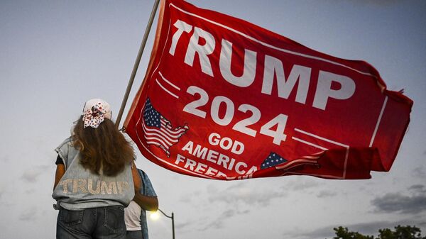 Una partidaria del expresidente estadounidense Donald Trump sostiene una bandera de 'Trump 2024' mientras protesta cerca del club Mar-a-Lago en Palm Beach, Florida, el 30 de marzo de 2023.  - Sputnik Mundo