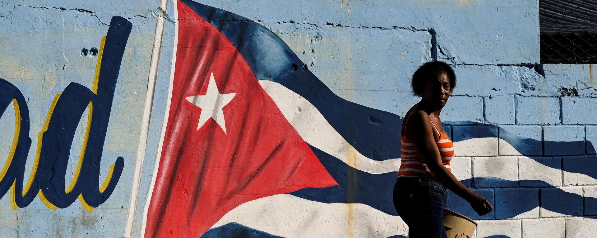 Una mujer pasa junto a un muro pintado con la bandera cubana con la leyenda Continuidad en La Habana, el 7 de febrero de 2023.  - Sputnik Mundo, 1920, 18.04.2023