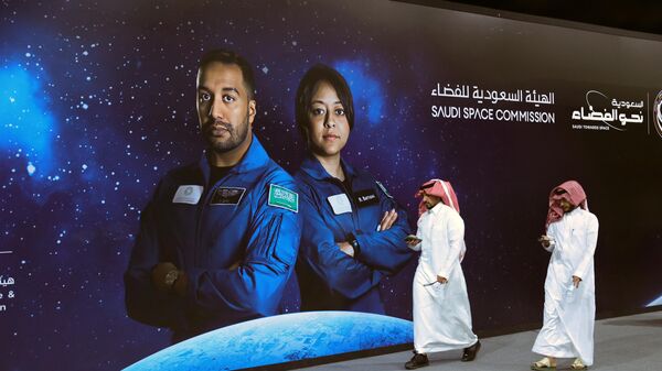 Un grupo de personas pasa junto a un cartel con la foto de los astronautas de la Comisión Espacial Saudita Ali Al-Qarni (izq.) y Rayyanah Barnawi, de la Misión Axiom 2, en una fiesta organizada por el gobierno en Riad el 21 de mayo de 2023.  - Sputnik Mundo