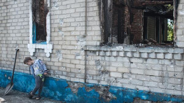 Un niño cerca de una casa destruida por los bombardeos en el pueblo de Aleksandrovka, región de Donetsk - Sputnik Mundo