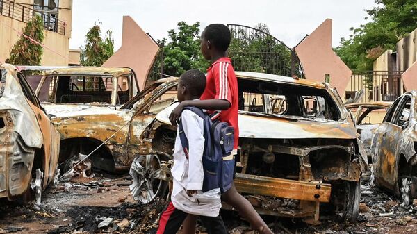 Niños caminan junto a unos coches quemados frente a la sede del Partido Nigerino para la Democracia y el Socialismo del presidente Bazoum, en Niamey, el 7 de agosto de 2023.  - Sputnik Mundo
