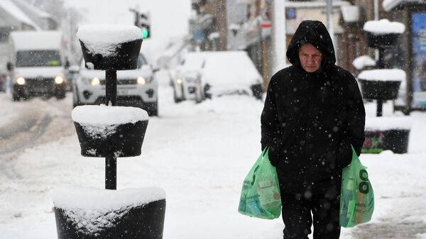 Un hombre lleva sus compras a través de la nieve en Escocia, el 18 de febrero de 2022 - Sputnik Mundo