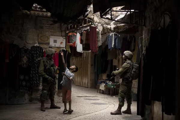 Un niño palestino jugando con un globo junto a soldados israelíes en un mercado cubierto de la ciudad cisjordana de Hebrón. - Sputnik Mundo