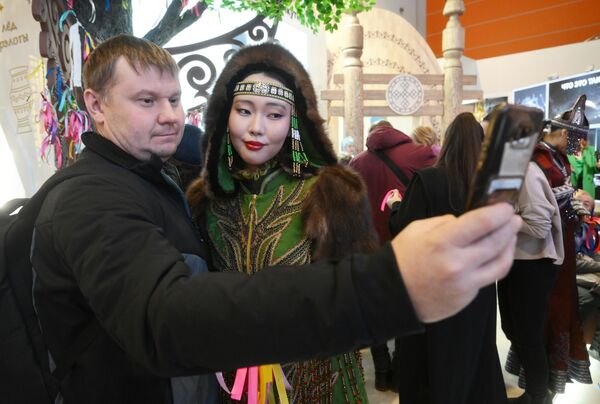 Un visitante tomándose una foto con una participante en un traje tradicional de los pueblos indígenas del Norte. - Sputnik Mundo