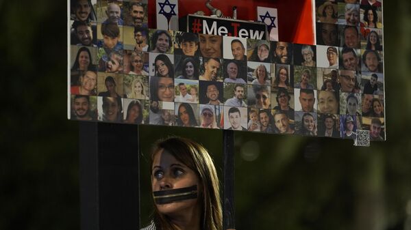 Una persona sostiene una pancarta con imágenes de los rehenes retenidos en la Franja de Gaza - Sputnik Mundo