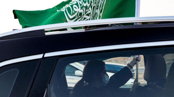 Una mujer sostiene una bandera nacional de Arabia Saudita desde la ventana de un vehículo mientras asiste a un espectáculo aéreo que marca las celebraciones del 93.º Día Nacional de Arabia Saudí en Riad el 23 de septiembre de 2023.  - Sputnik Mundo