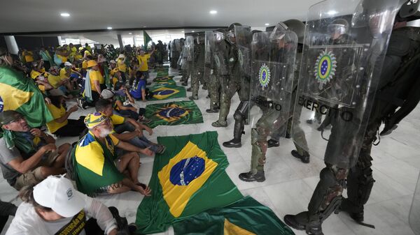Simpatizantes del expresidente de Brasil, Jair Bolsonaro, se sientan frente a una línea de policías militares dentro del palacio presidencial de Planalto tras irrumpir en el lugar de trabajo oficial del mandatario, en Brasilia, Brasil, el 8 de enero, 2023 - Sputnik Mundo