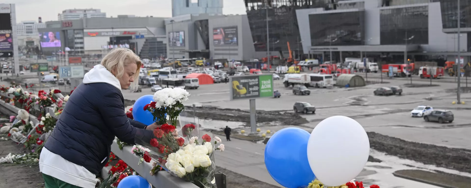 Una mujer deposita flores en un monumento espontáneo en la carretera frente a la sala de conciertos Crocus City Hall, donde se produjo el tiroteo y el incendio - Sputnik Mundo, 1920, 27.03.2024