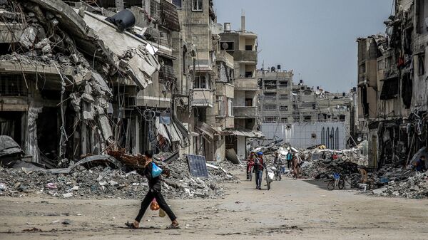 Un niño camina con bolsas de alimentos  cerca de edificios destruidos en la ciudad de Gaza el 27 de marzo de 2024. - Sputnik Mundo