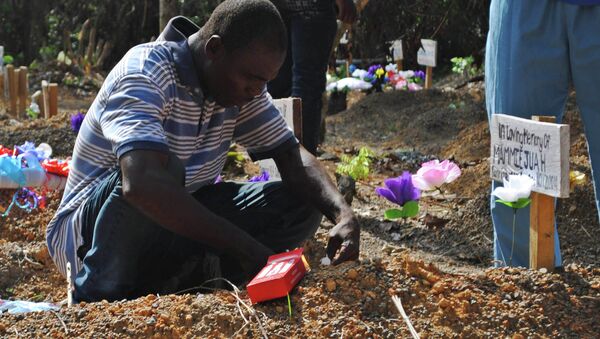 Sobreviviente del virus Ébola Stanley Juah llora en la tumba de su hijo en un cementerio para las víctimas de Ébola - Sputnik Mundo