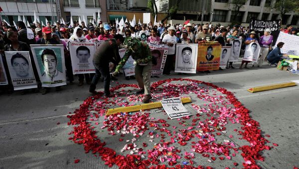 A man spreads rose petals in the shape of a heart as relatives hold up posters of some of the 43 missing students of the Ayotzinapa Teacher Training College - Sputnik Mundo