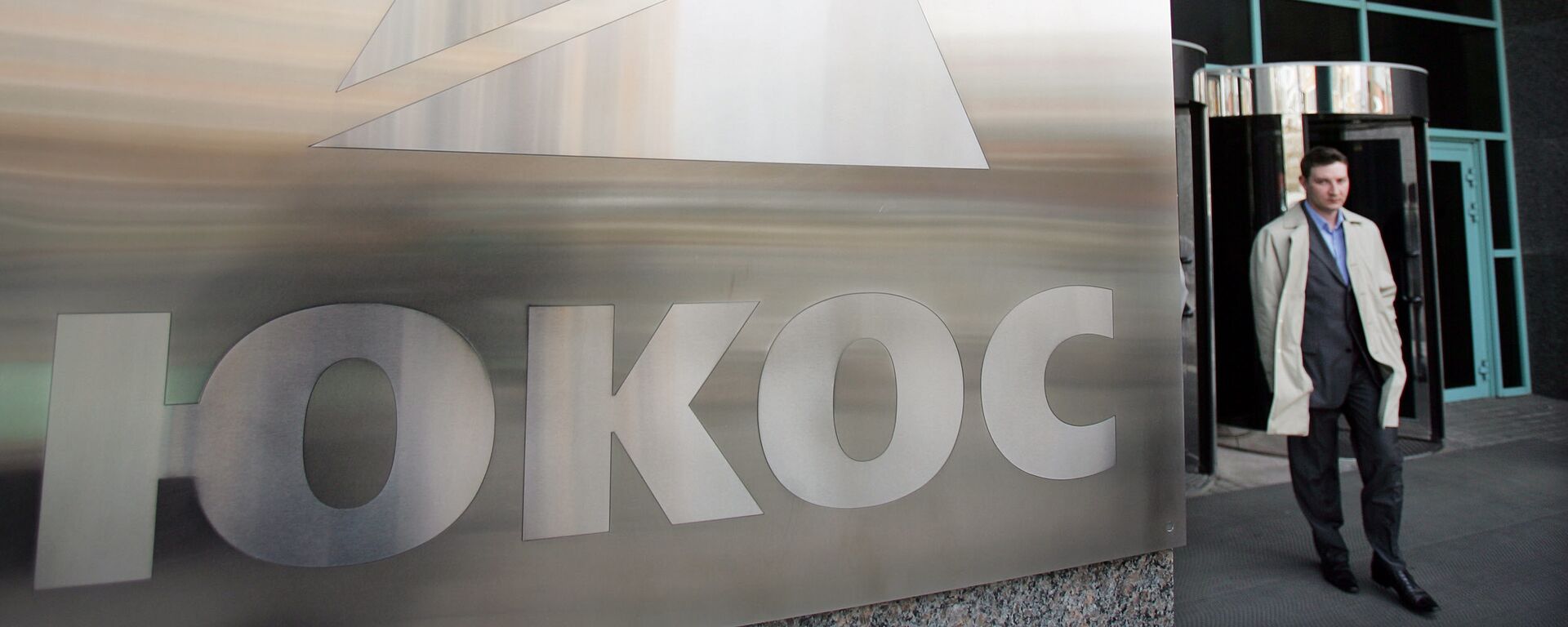 A man passes by a Yukos logo at the headquarters of the oil company in Moscow after the latest auction for the sale of package of assets the stricken giant, 04 April 2007 - Sputnik Mundo, 1920, 29.07.2021