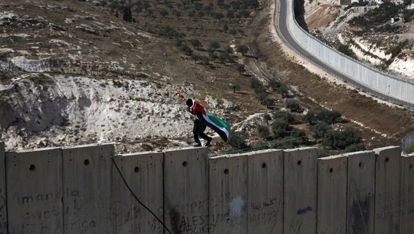 Un palestino camina sobre el muro de Cisjordania, construido por Israel - Sputnik Mundo
