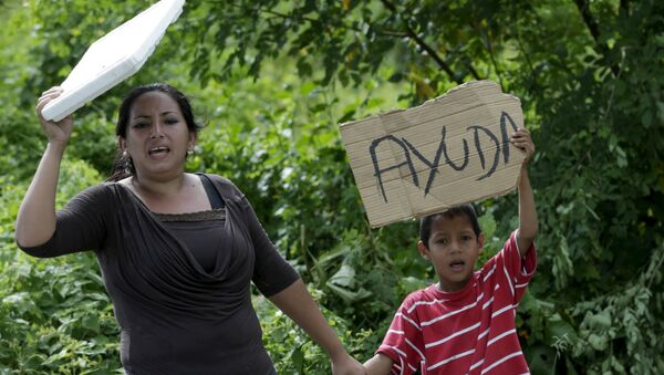 Local residents hold up a poster along a road near the village of Canoa - Sputnik Mundo