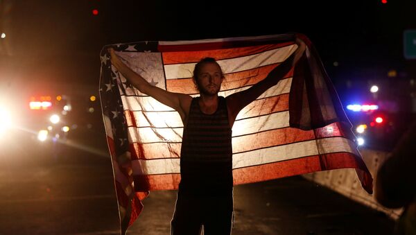 Un manifestante con la bandera de EEUU durante protestas tras la victoria de Donald Trump - Sputnik Mundo