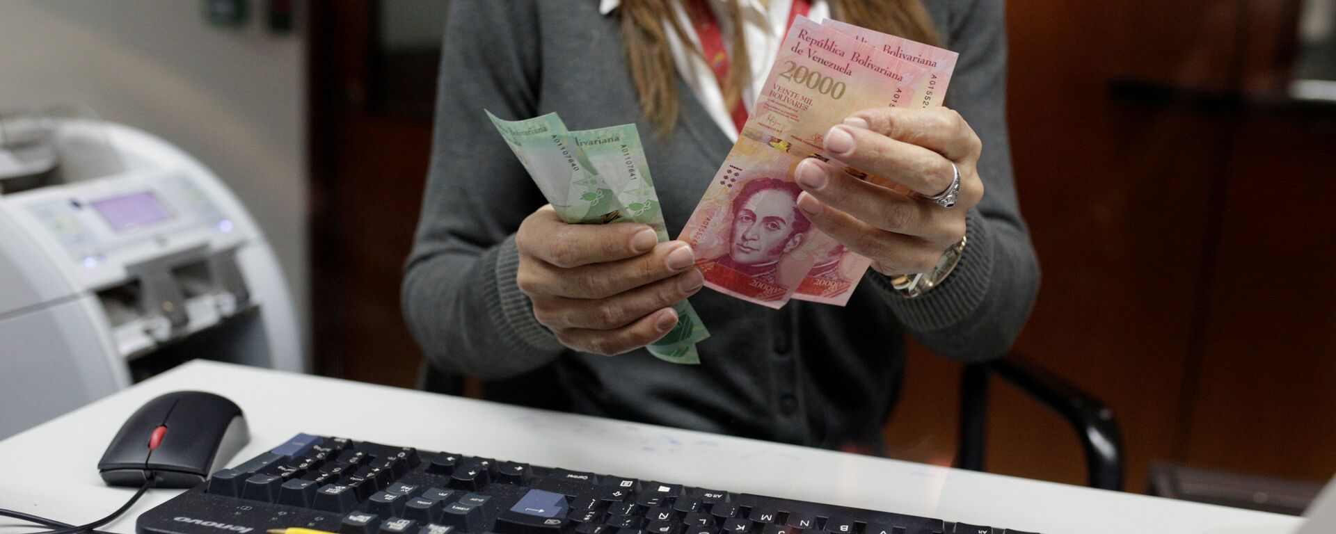 A bank teller counts bolivar banknotes at a Banco de Venezuela branch in Caracas - Sputnik Mundo, 1920, 21.01.2021