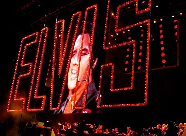 Elvis Presley cantando como su banda en el inicio del Concierto dedicado al 25º Aniversario de Elvis Presley en Memphis, Tennessee. El signo rojo de Elvis se usa a partir de su 'gira de regreso' de 1968. - Sputnik Mundo