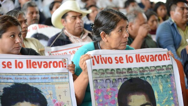 Personas sostienen carteles que recuerdan a los 43 desaparecidos de Ayotzinapa, en una visita de la Comisión Interamericana de Derechos Humanos a la escuela normal en la que estudiaban, en 2015. - Sputnik Mundo