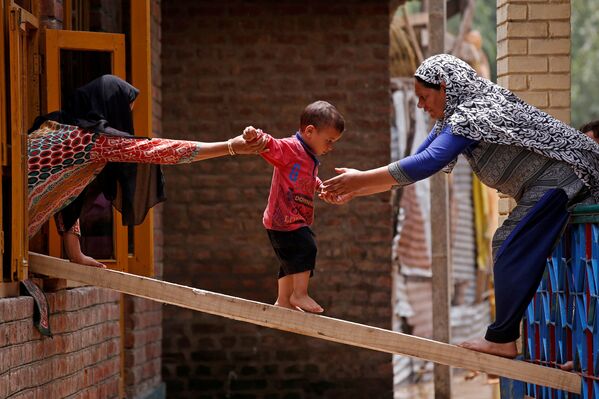 Dos mujeres hindúes ayudan a un niño a cruzar de una casa a otra durante una inundación. - Sputnik Mundo