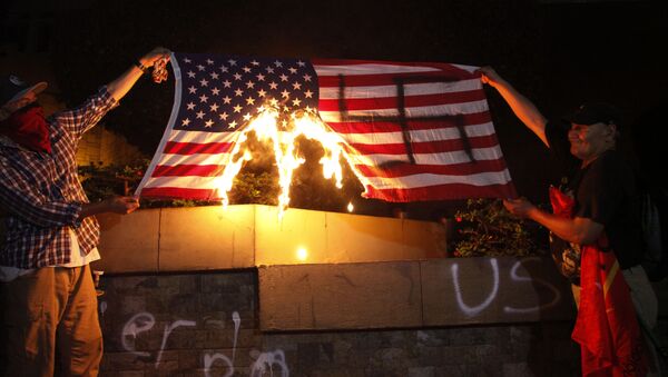 Dos personas están quemando una bandera de Estados Unidos durante una protesta a favor de la caravana de migrantes frente a la embajada estadounidense en Tegucigalpa, Honduras - Sputnik Mundo