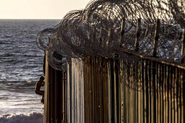 Dos jóvenes se suben al muro de playas de Tijuana después de que el Ejército estadounidense colocara alambre de púas el 13 de noviembre del 2018 - Sputnik Mundo